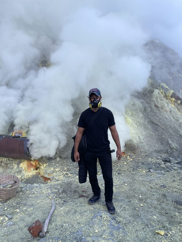 Majdi Alassaf wearing a black and yellow respirator mask inside the Kawah Ijen crater, sulfur smoke around him